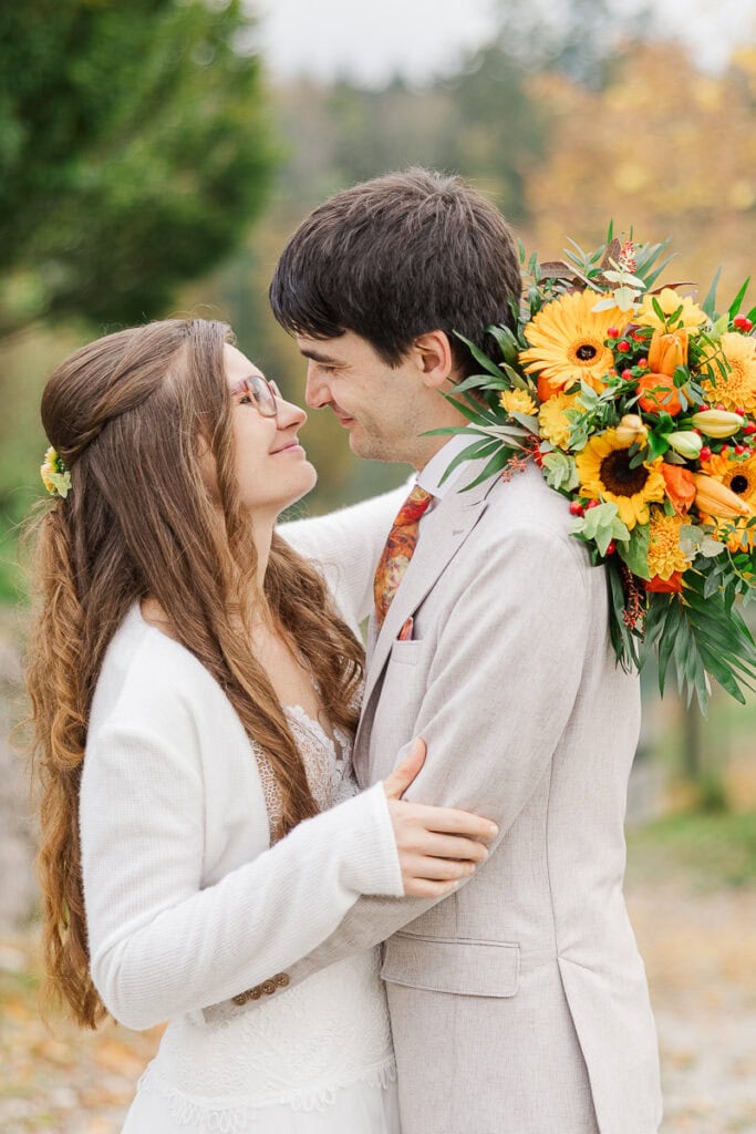 Lächelndes Hochzeitspaar mit Sonnenblumenstrauß im Herbst.