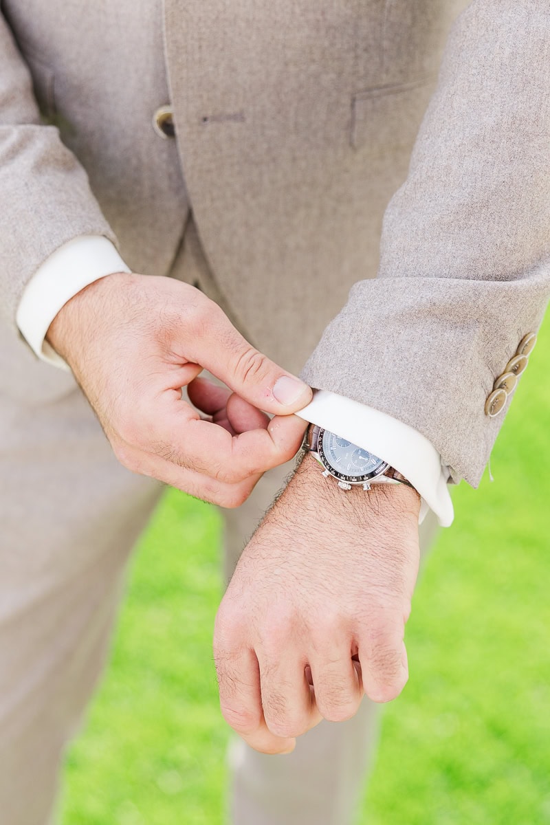 Mann richtet Jackettärmel, Armbanduhr sichtbar.