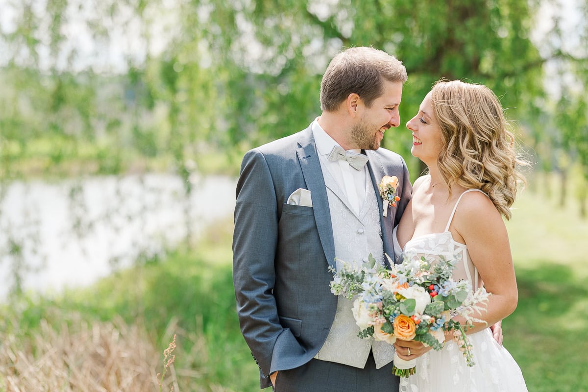 Lächelndes Brautpaar im Freien mit Blumenstrauß.